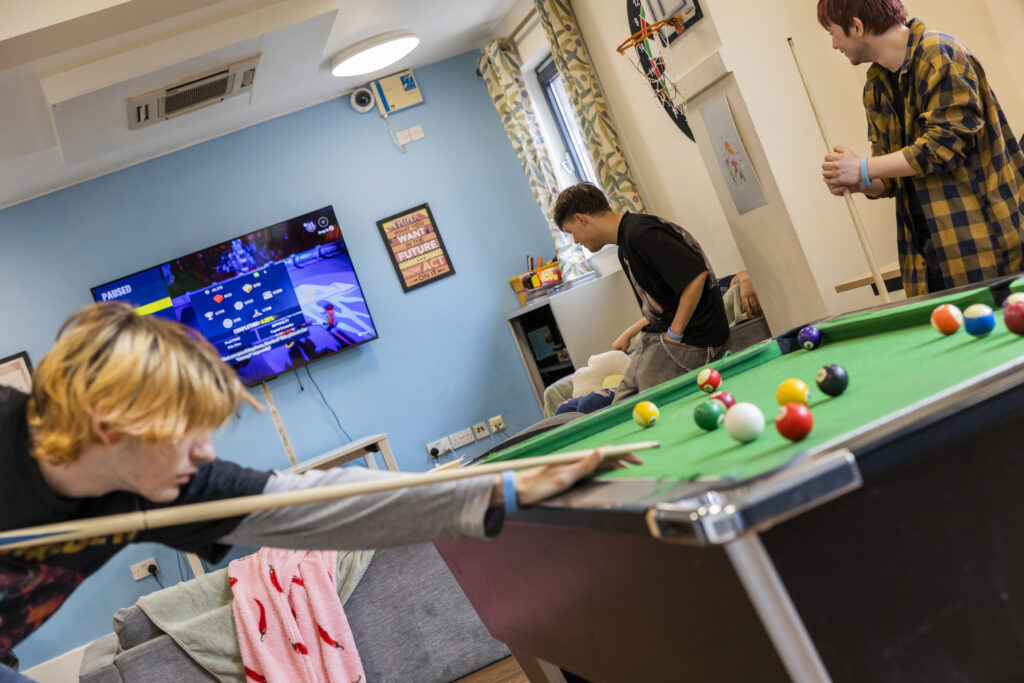 Young people playing pool in the communal area of YMCA Norfolk supported accommodation